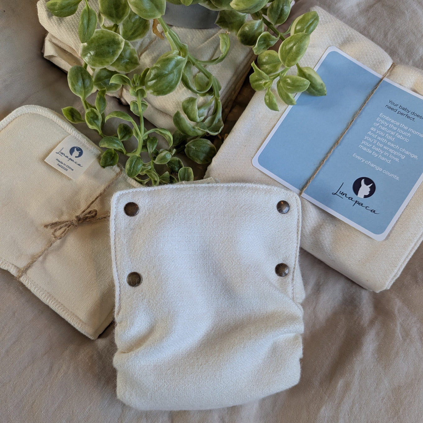 Set of reusable diapers with a plant and branded card on a linen cloth background