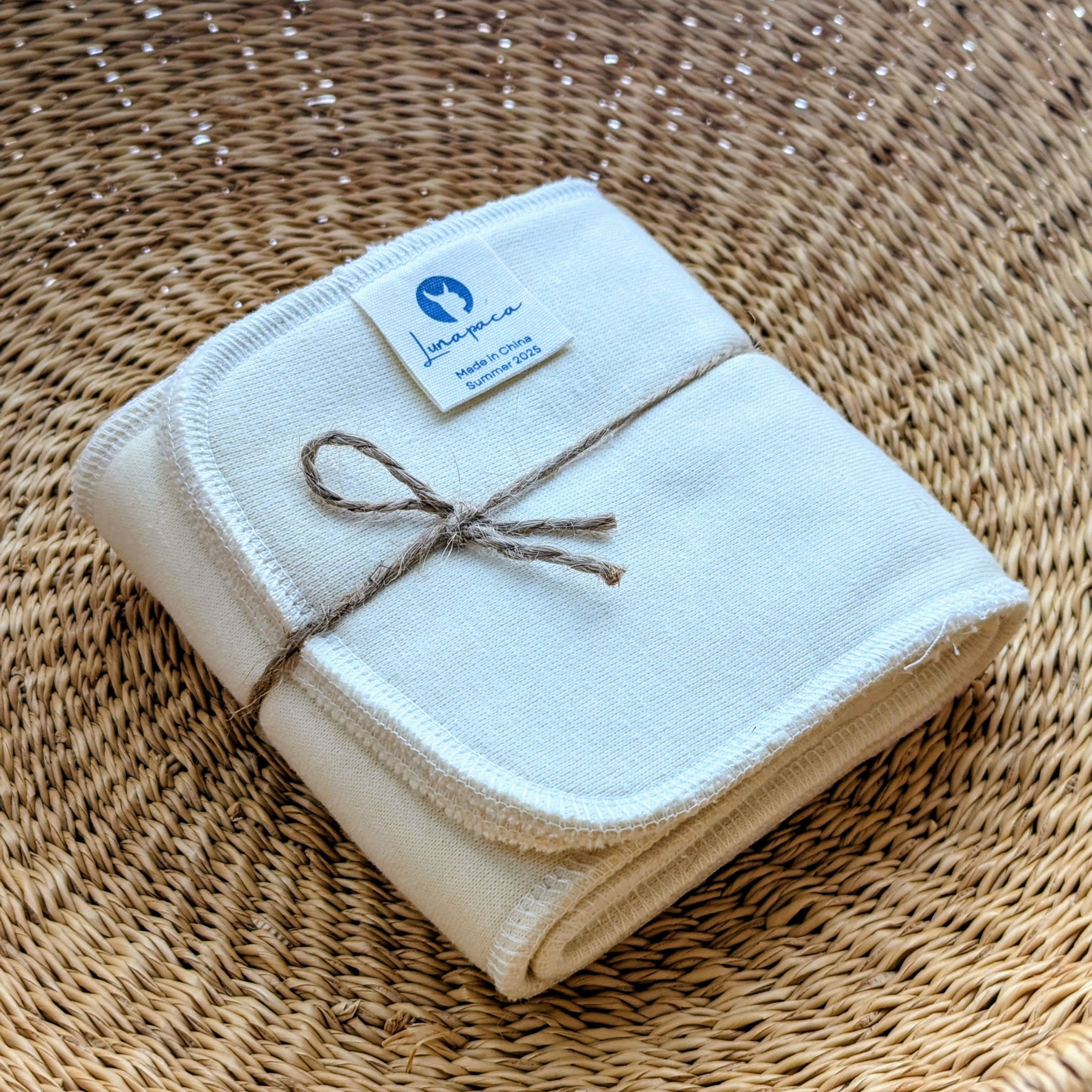 2 folded pads with a label tied together with twine inside a woven basket.