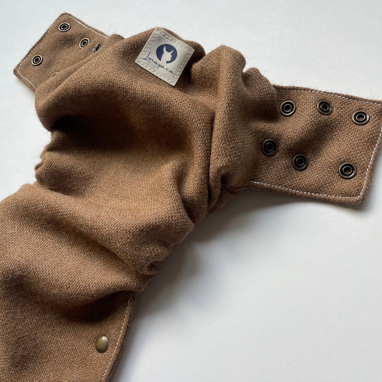 A dark brown alpaca diaper cover with brass side snaps and cotton white logo tag with an alpaca silhouette lays open on a white background.