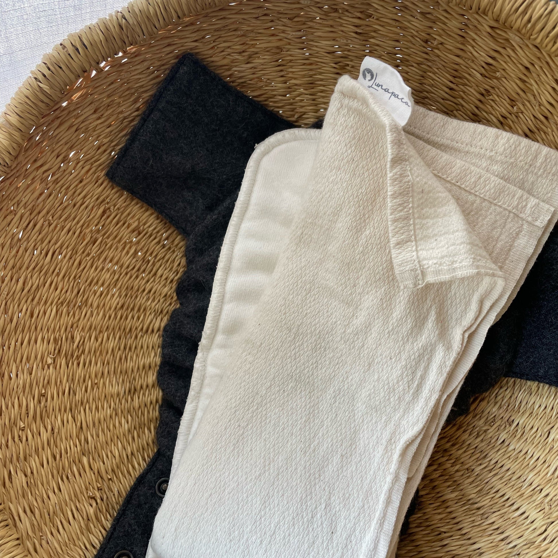 Close up of hemp booster between cotton flat and alpaca diaper cover inside a woven basket.