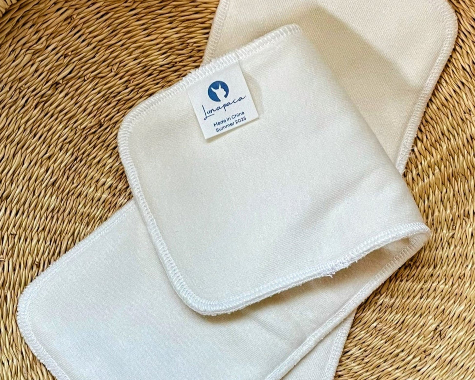 Two white cloth pads on a woven basket on a wooden surface