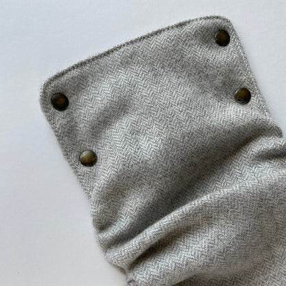 The front panel of an alpaca diaper cover with a white and light gray mini herring bone weave featuring 4 brass snaps on top of a white background.