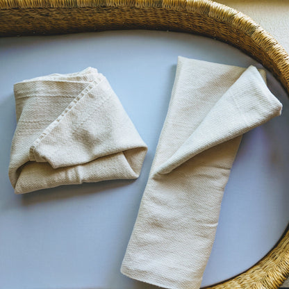 2 cotton flats diapers on a diaper changing basket, the first flat diaper is folded into a diaper shape called an "origami fold", the second flat diaper is folded into a rectangle shape called a "pad fold".