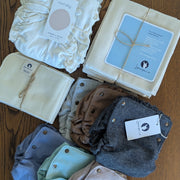cotton inners, flat diapers, hemp booters, and a variety of alpaca diaper covers in a mix of colors on a wooden table.