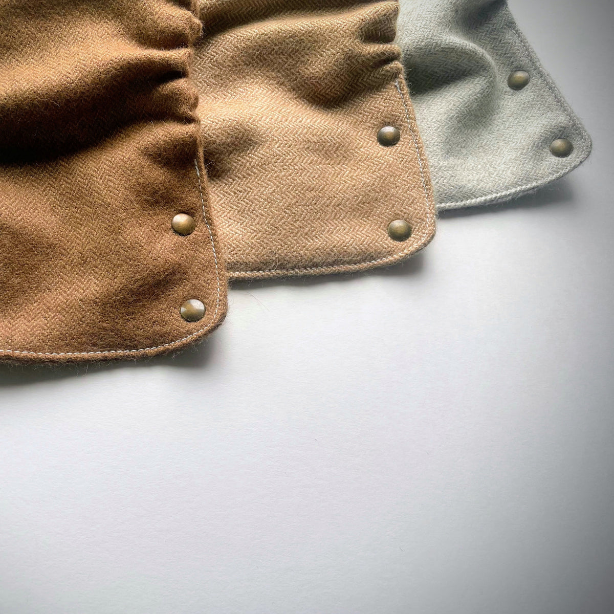 Brown, tan, and light gray alpaca diaper covers with brass snaps on a white background