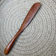 A wooden Wipe-Away Wand for easy cloth diaper cleaning and solid waste removal, resting on a natural woven mat.