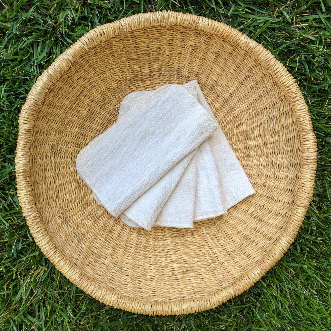 Soft organic cotton cloth baby wipes from Lunapaca folded in a woven basket resting on green grass for a natural, zero-waste routine.